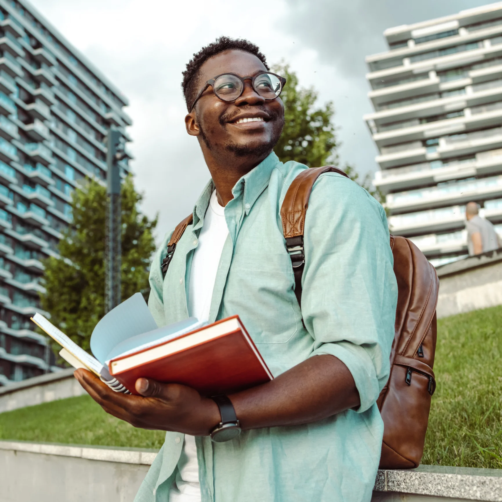 Smiling person holding books outdoors, wearing backpack.